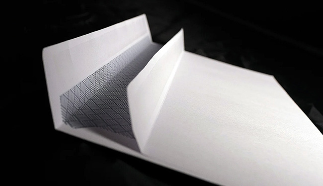Open white 100gsm self-seal wallet flap custom printed envelope by TradePrintingUK.com on black background, featuring gummed flap with hatched pattern for secure closure and blank panels for addressing business mail in DL size.