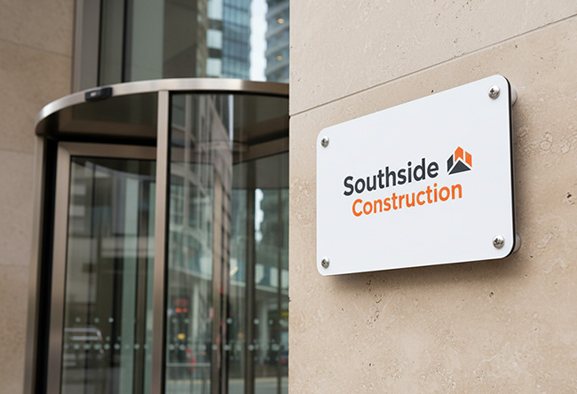 Outdoor DiBond sign printed by TradePrintingUK.com, mounted with standoffs on stone wall next to a glass revolving door, showing Southside Construction logo with grey and orange text, designed for durable, professional business signage in construction or trade environments.